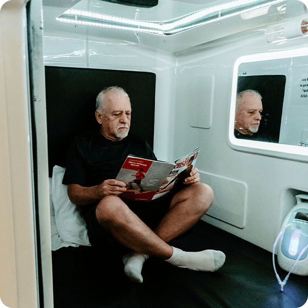 Male patient reading magazine while sitting in the Hyperbaric Cube Chamber