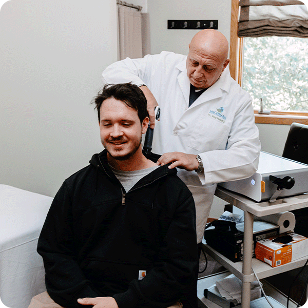 Doctor Tony applies shockwave therapy tool to male patient's neck and shoulder
